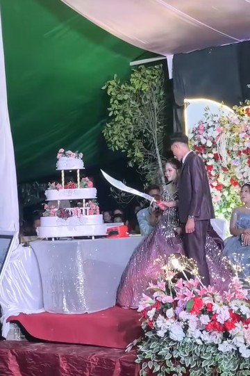 Aksi unik pasangan pengantin memotong kue pernikahan bertingkat memakai sebilah pedang panjang bikin heboh di Manado, Sulawesi Utara. Foto: Dok. TikTok @dionmundung31.