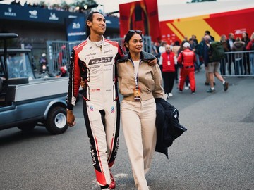 Momen manis tercipta saat Sean Gelael yang mengenakan baju balap lengkap tim WRT, berjalan bergandengan tangan dengan Hana Malasan di area pit lane. Hana tampil chic dan santai mengenakan atasan lengan panjang merah muda pastel, rok pendek putih, kacamata hitam, dan tas tangan kecil berwarna merah tua. (Foto: dok Instagram hanamalasan)