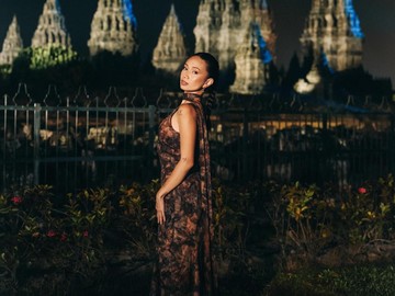 NIKI tampil mempesona berdiri tegak menghadap kamera dengan latar belakang kemegahan Candi Prambanan yang diterangi lampu sorot biru dan kuning. Ia menawan dalam balutan sleeveless long dress bermotif abstrak dengan nuansa warna bumi. (Foto: dok Instagram nikizevanya)